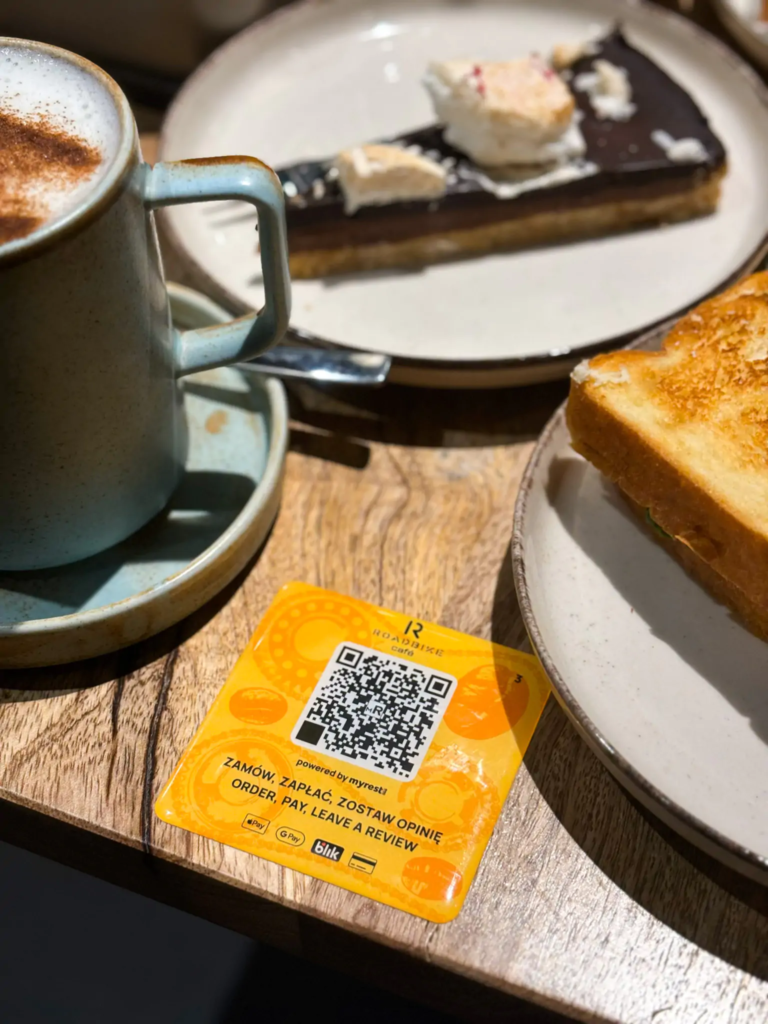 Kawa, ciasto czekoladowe i tost na stoliku z kartą z kodem QR do zamawiania i płatności.