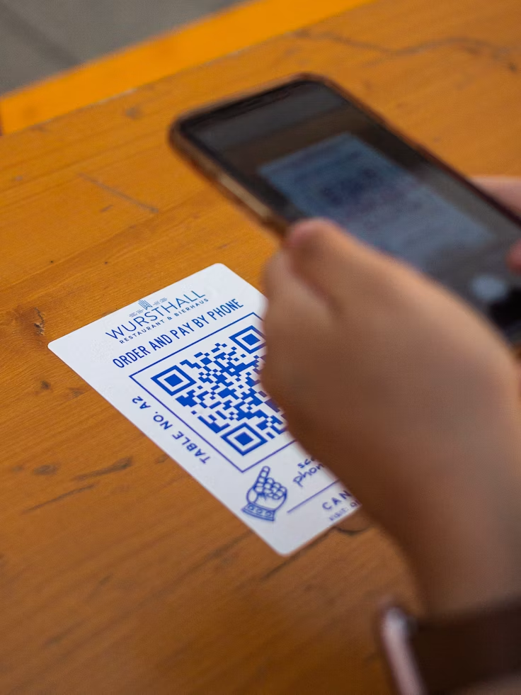 Osoba skanuje telefonem kod QR umieszczony na stoliku w restauracji.